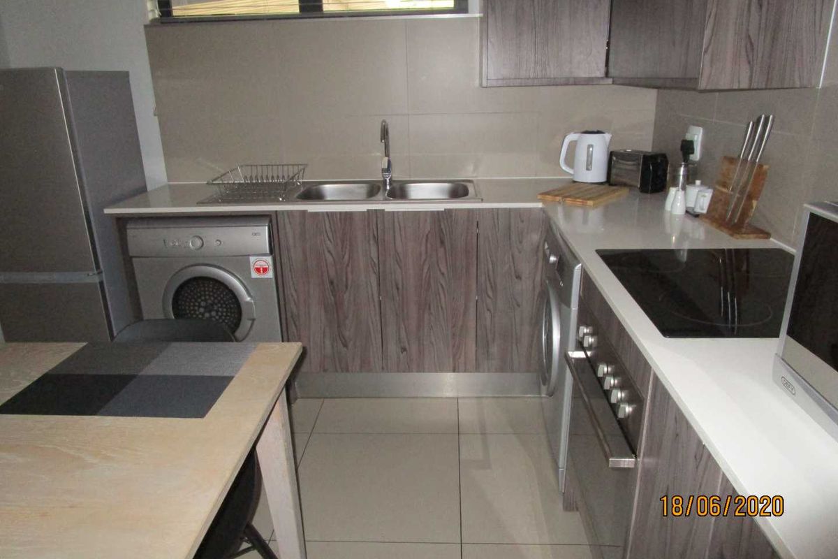 Modern kitchen featuring wood-grain cabinetry, stone countertops, integrated electric hob and oven, and tiled splashbacks.