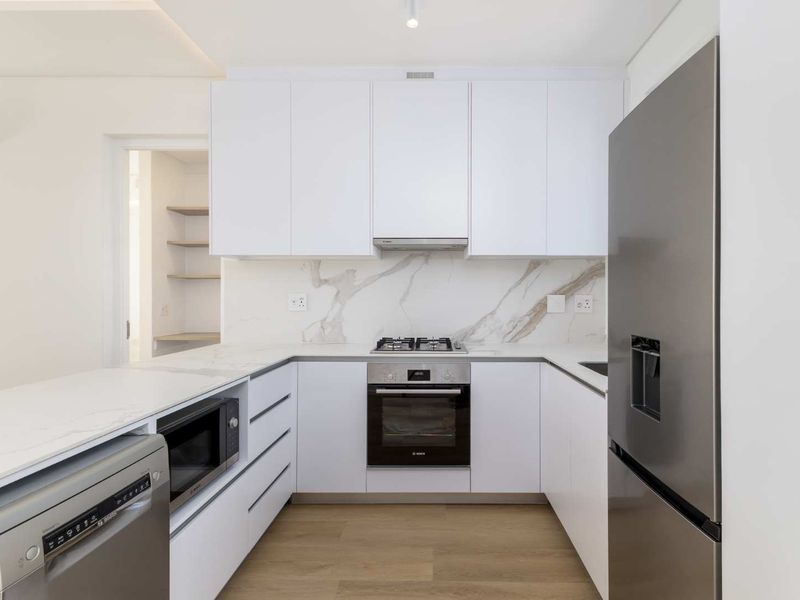 Modern kitchen featuring sleek white cabinetry, marble-look splashback, stone countertops, and high-quality built-in appliances, including a gas hob and oven.