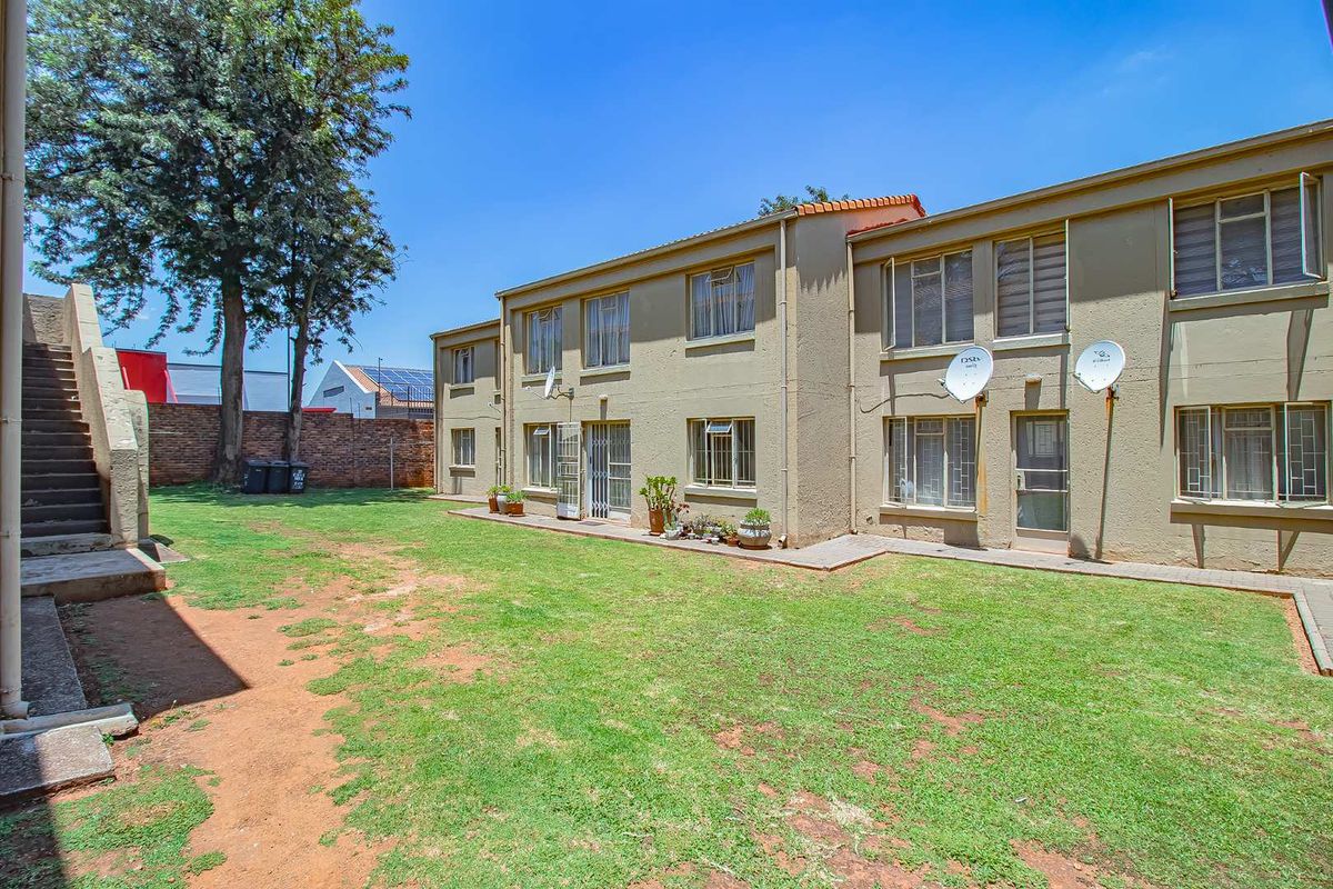 Rear view of the apartment complex featuring a communal lawn, paved walkways, and exterior access staircases.