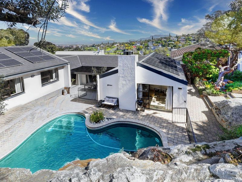 Elevated view of a rear garden featuring a swimming pool, paved patio area, and a house with solar panels installed on the roof.