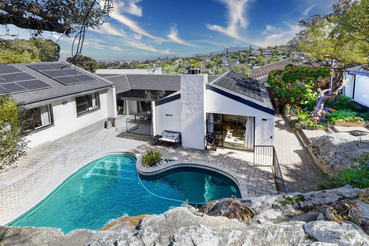 Elevated view of a rear garden featuring a swimming pool, paved patio area, and a house with solar panels installed on the roof.