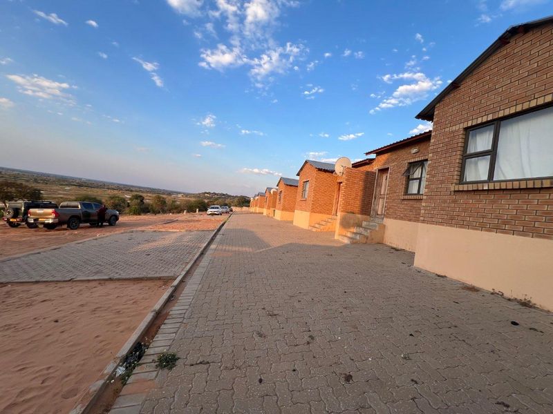 Exterior view of a row of brick townhouse units featuring paved driveway access and open landscape surroundings.