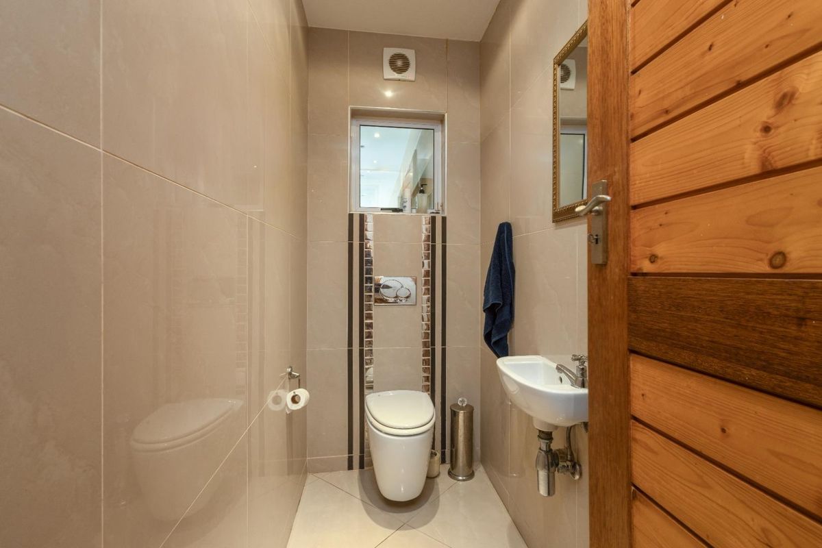 A compact guest bathroom featuring floor-to-ceiling tiling, a wall-mounted toilet with a chrome flush plate, and a small wall-mounted basin.