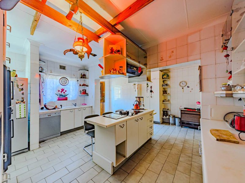 A dated kitchen featuring a central island with a built-in hob, tiled flooring, and exposed timber ceiling beams, offering significant potential for modernization.