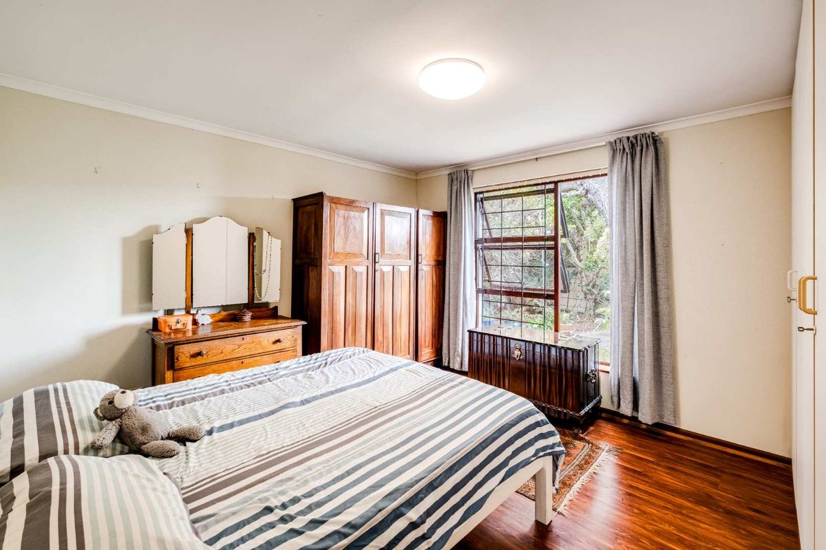 A well-lit bedroom featuring laminate flooring, built-in cupboards, and a steel-framed window with security bars overlooking the garden.