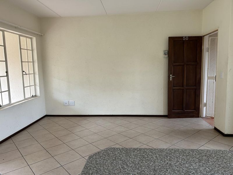An empty living area featuring tiled flooring, a timber entrance door, and a steel-framed window, offering a blank canvas for personalization.