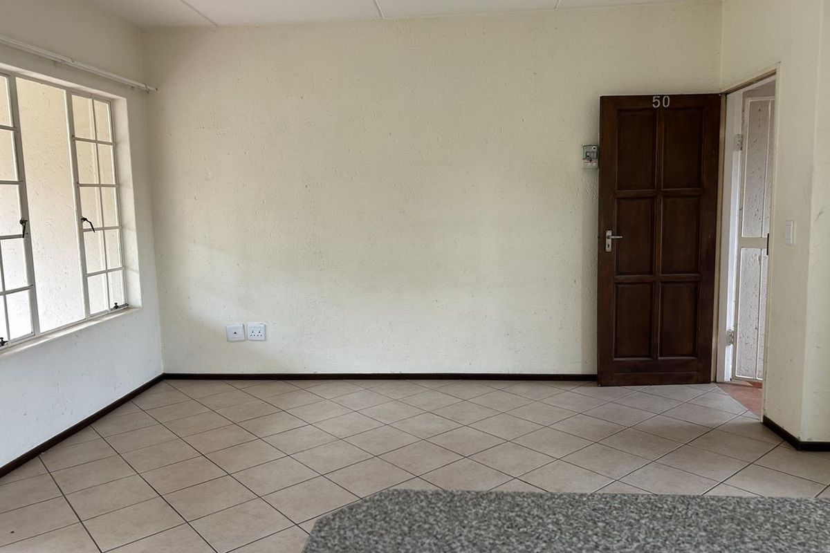 An empty living area featuring tiled flooring, a timber entrance door, and a steel-framed window, offering a blank canvas for personalization.