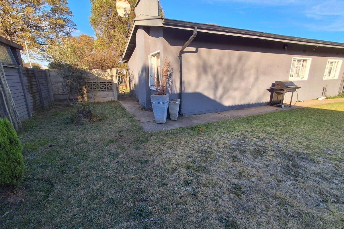 Rear exterior view of the house featuring a concrete pathway, precast boundary wall, and chimney stack set against a lawn area.