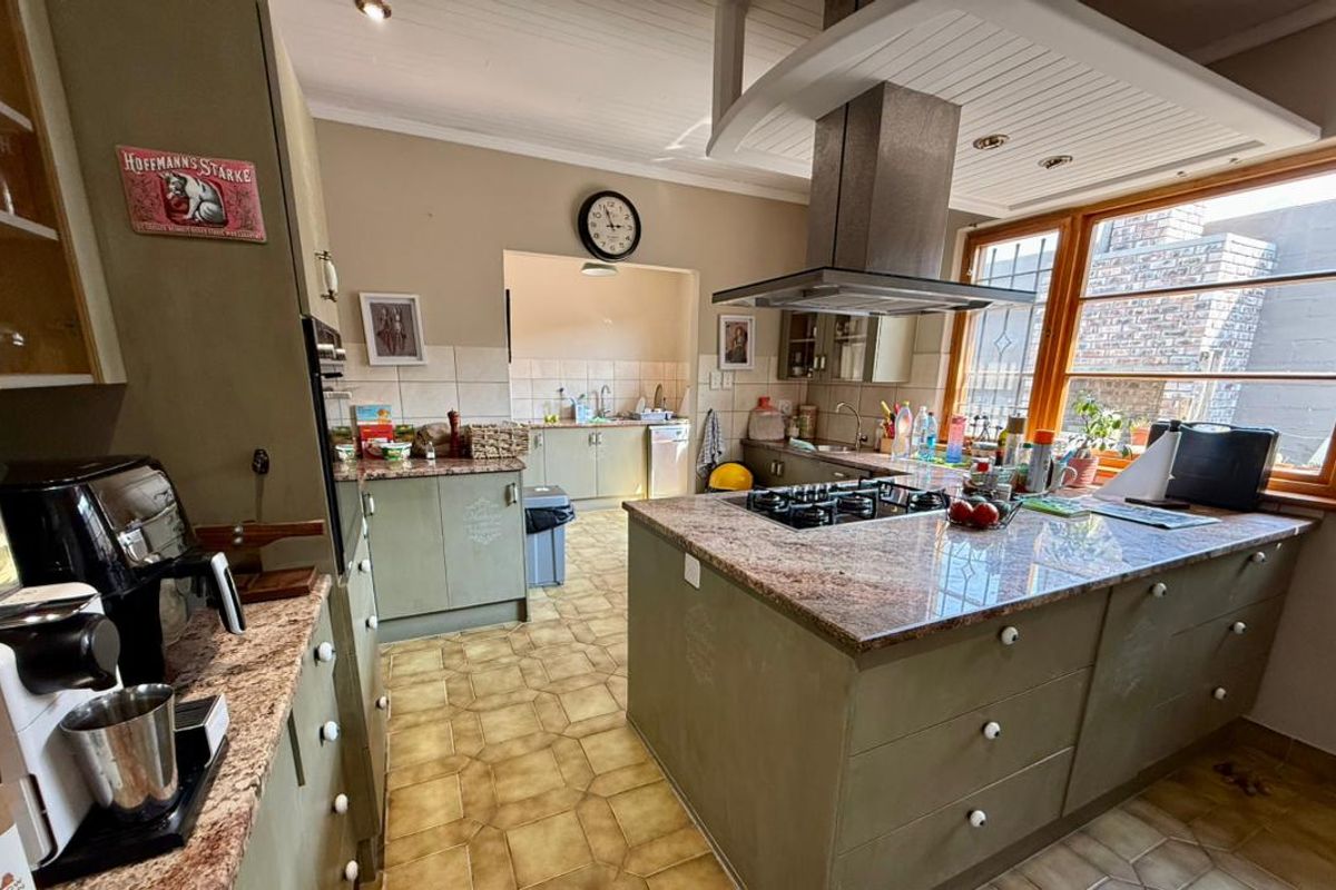 Spacious kitchen featuring granite countertops, a central island with a gas hob, stainless steel extractor fan, and ample wooden cabinetry.