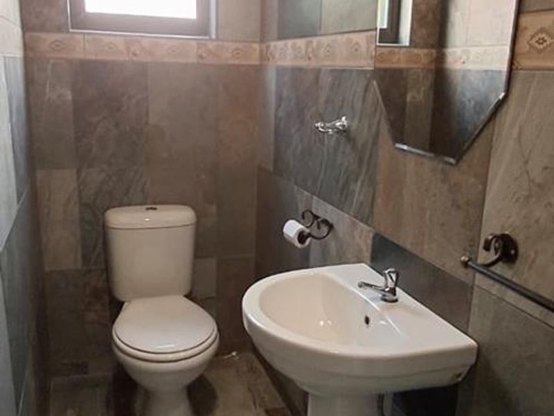 A compact bathroom featuring full-height wall tiling, a pedestal basin, and a standard toilet, finished with neutral floor tiles.