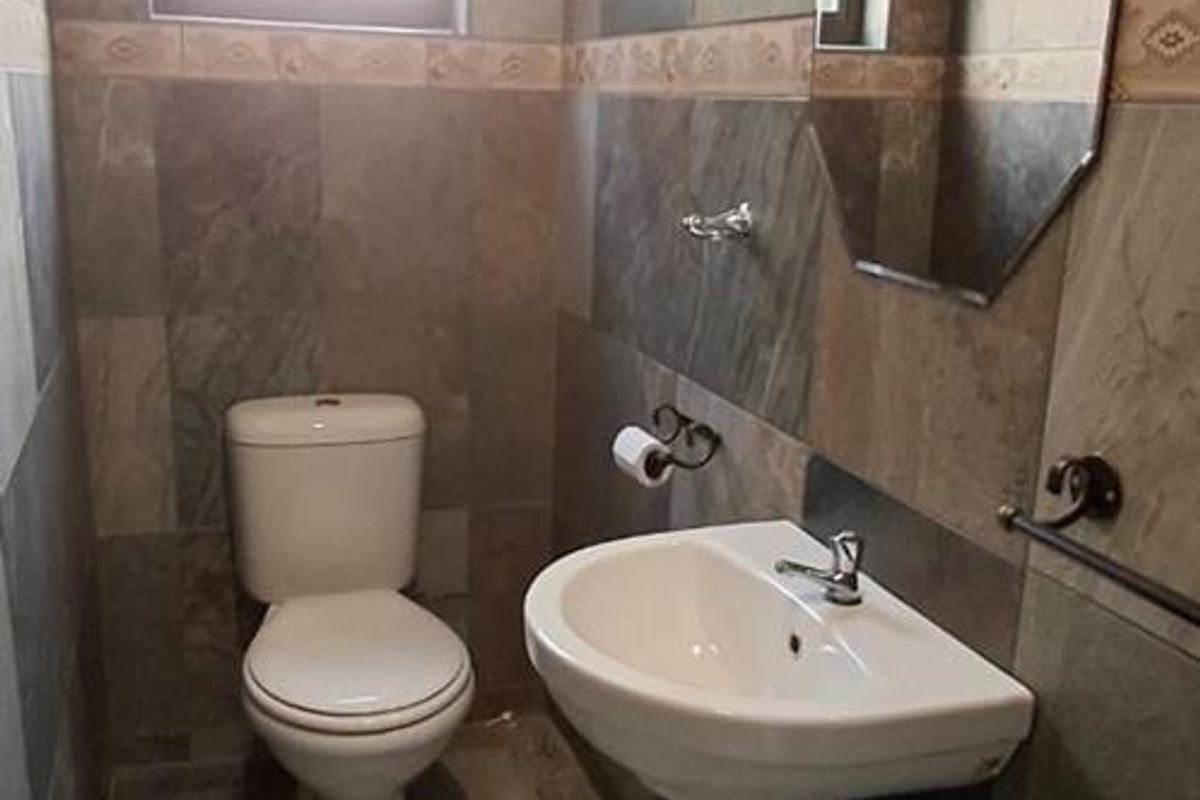 A compact bathroom featuring full-height wall tiling, a pedestal basin, and a standard toilet, finished with neutral floor tiles.