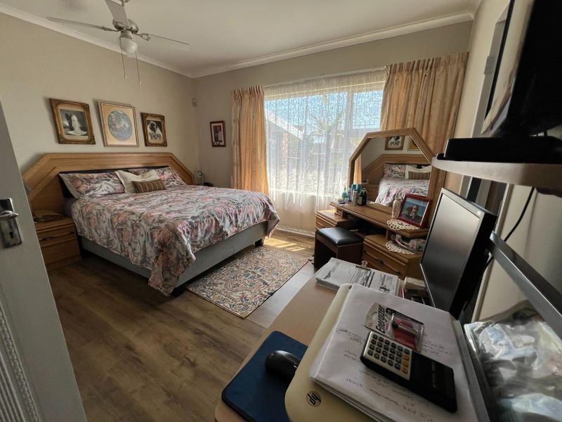 A well-lit bedroom featuring laminate flooring, a ceiling fan, and a large window with natural light.