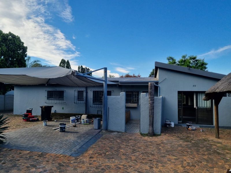 Rear exterior view of the house featuring a paved patio area, shade sail, and sliding door access to the interior.