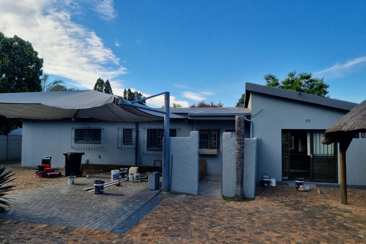 Rear exterior view of the house featuring a paved patio area, shade sail, and sliding door access to the interior.
