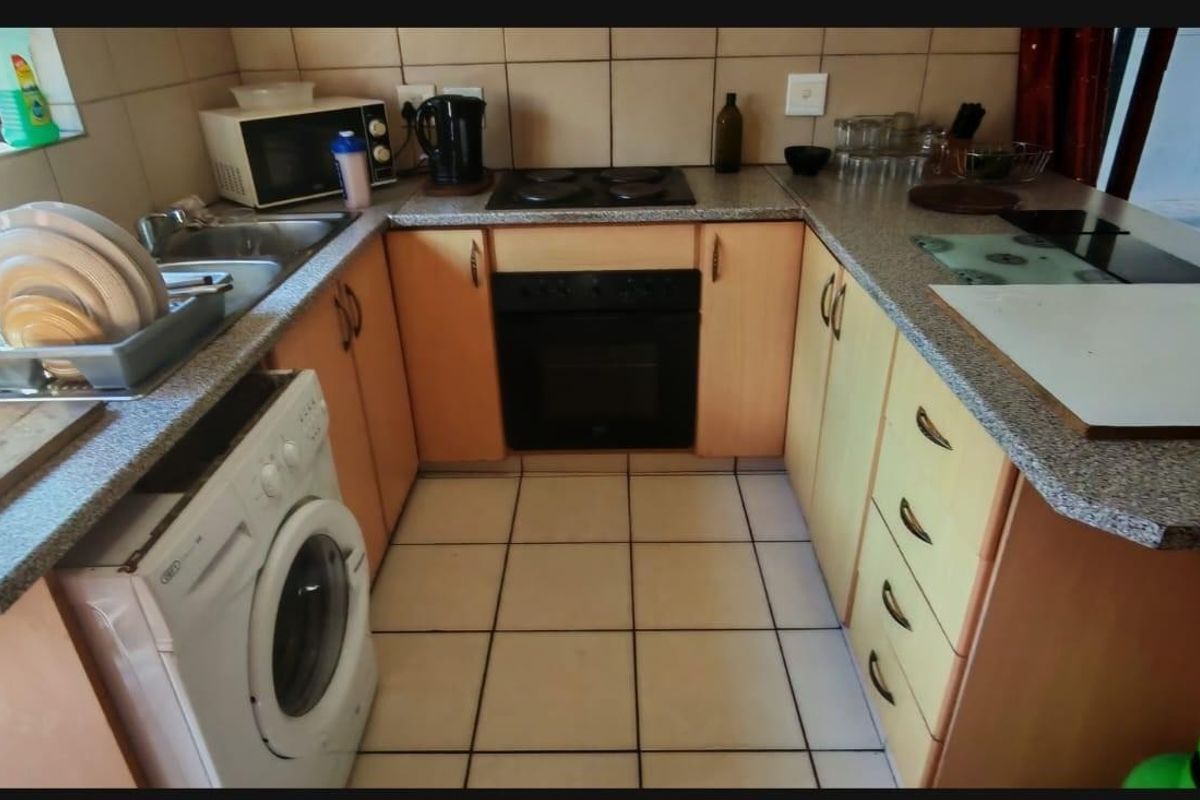 A compact kitchen featuring built-in cabinetry, laminate countertops, a built-in oven with electric hob, and tiled flooring and backsplash.