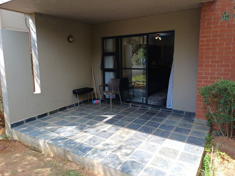 A covered patio area featuring slate tile flooring and a sliding glass door entrance, providing a functional outdoor space for relaxation.