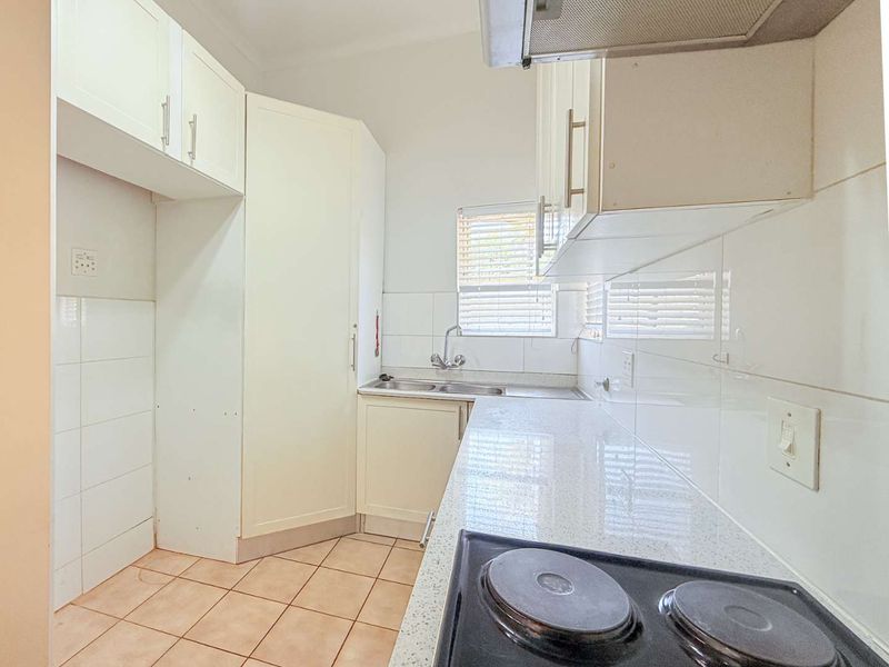 A functional kitchen featuring white cabinetry, stone countertops, a double sink, and a built-in electric hob with an extractor fan.