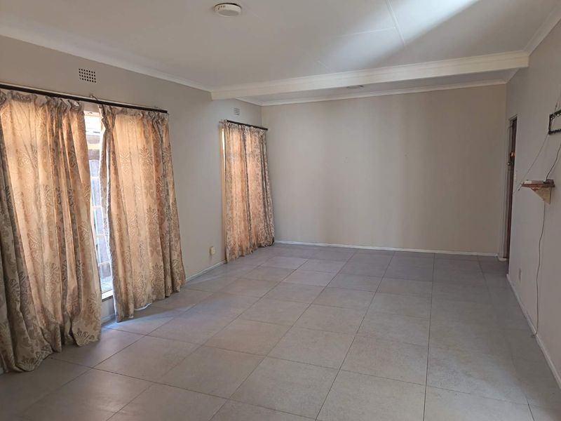 A spacious, empty living room featuring neutral wall tones, tiled flooring, and classic ceiling cornicing, offering a blank canvas for interior design.