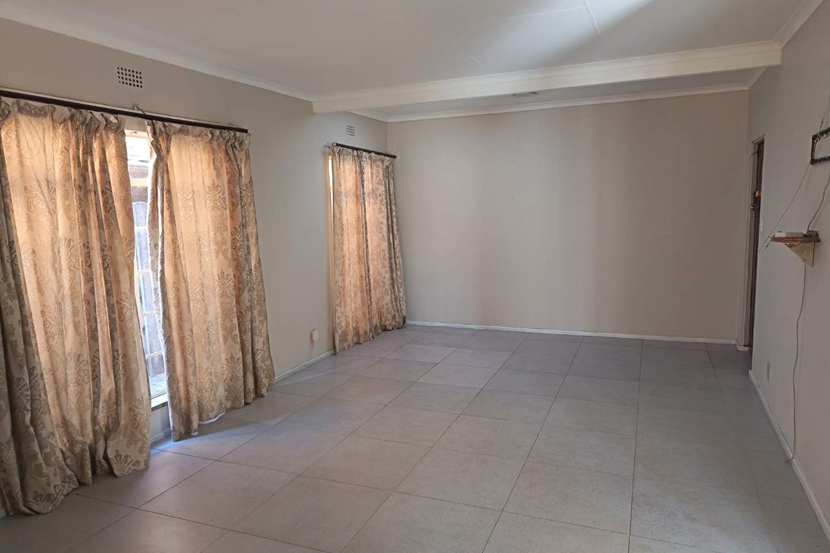 A spacious, empty living room featuring neutral wall tones, tiled flooring, and classic ceiling cornicing, offering a blank canvas for interior design.
