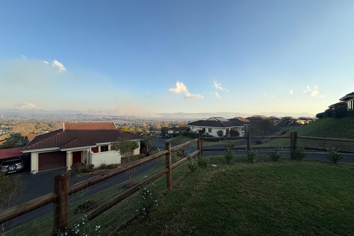An elevated view overlooking a residential townhouse estate with landscaped lawns, post-and-rail fencing, and distant mountain vistas.