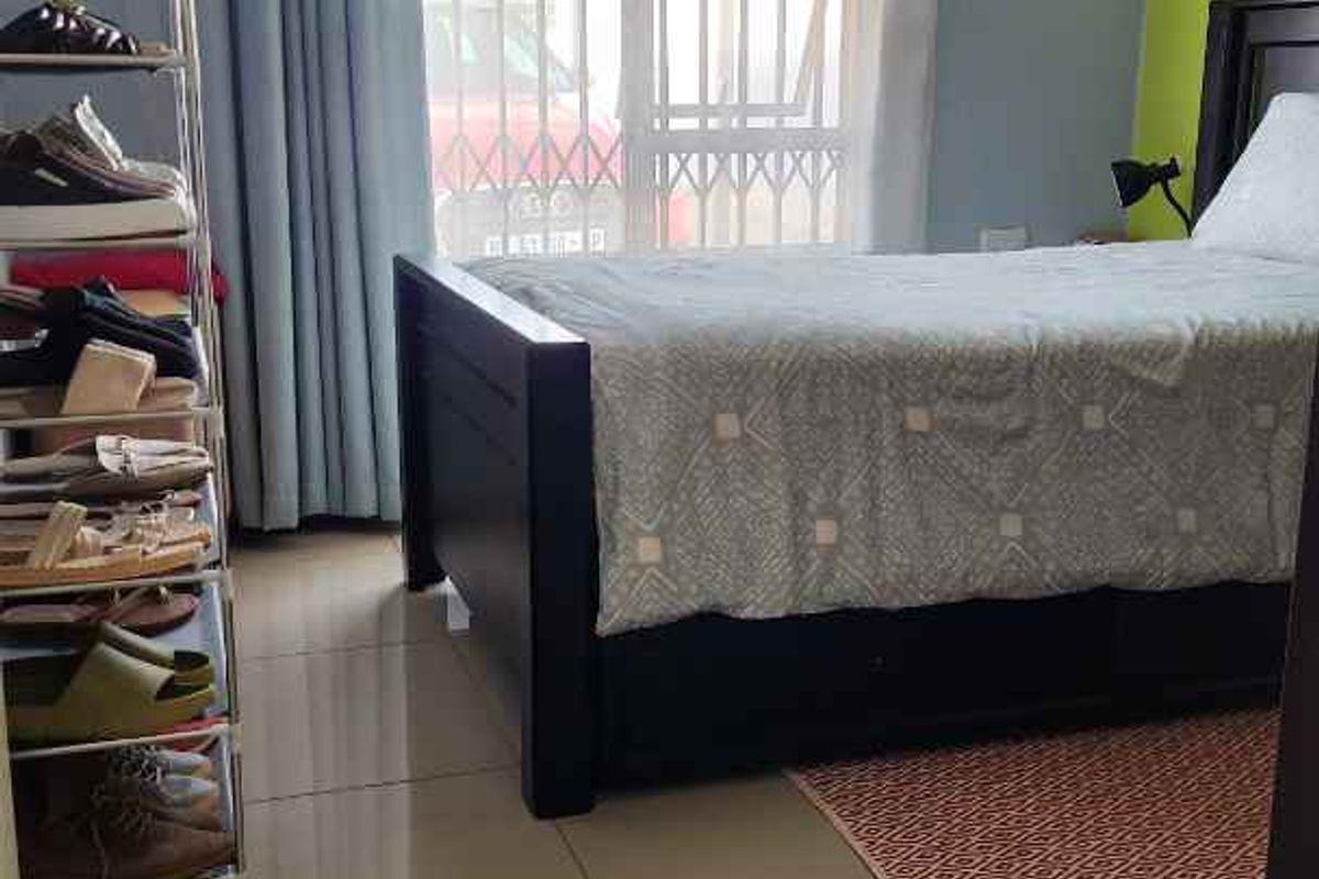 A bedroom featuring large format floor tiles, a window with security bars, and a neutral color palette with an accent wall.