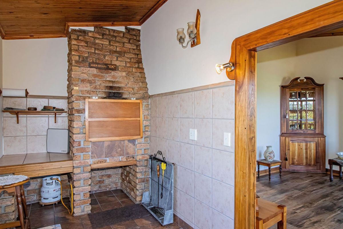 Indoor braai area featuring a built-in brick fireplace, tiled splashbacks, and wooden ceiling finishes, leading into an adjacent living space.