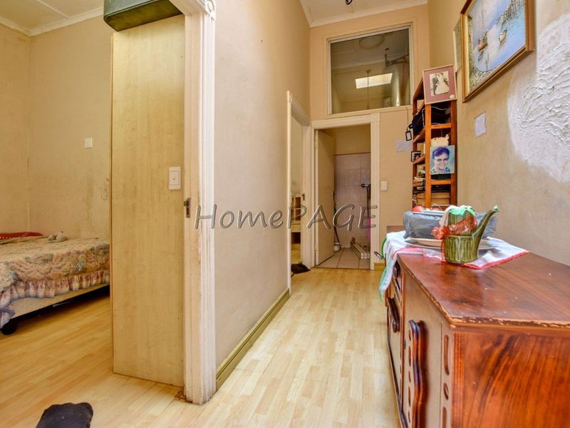 A view through a hallway leading to a bedroom and bathroom, featuring laminate flooring and dated wall finishes in need of maintenance.