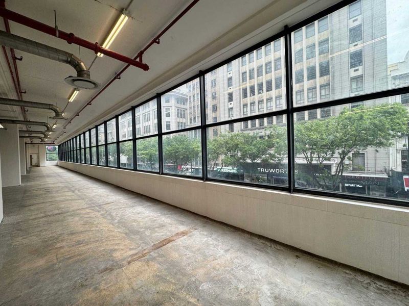 Spacious open-plan retail or office area featuring large windows, exposed industrial ceiling services, and concrete flooring with an urban street view.