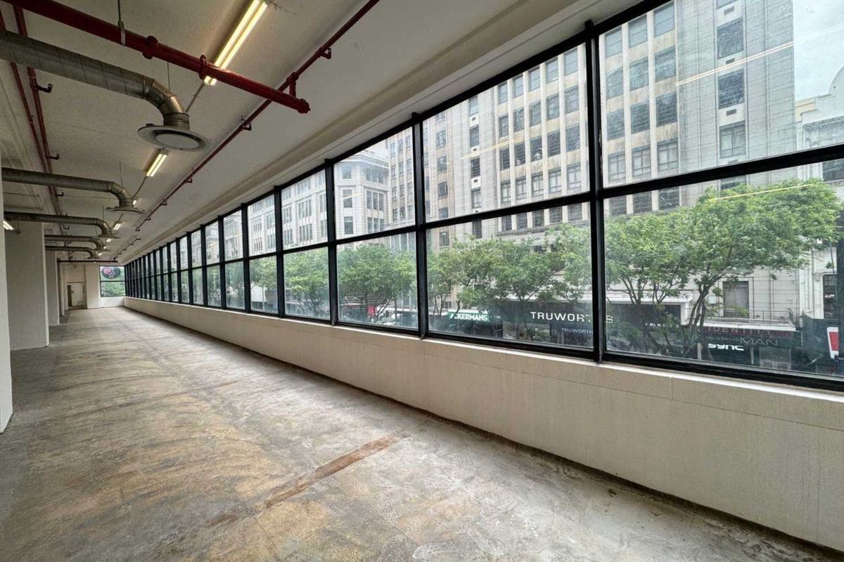 Spacious open-plan retail or office area featuring large windows, exposed industrial ceiling services, and concrete flooring with an urban street view.