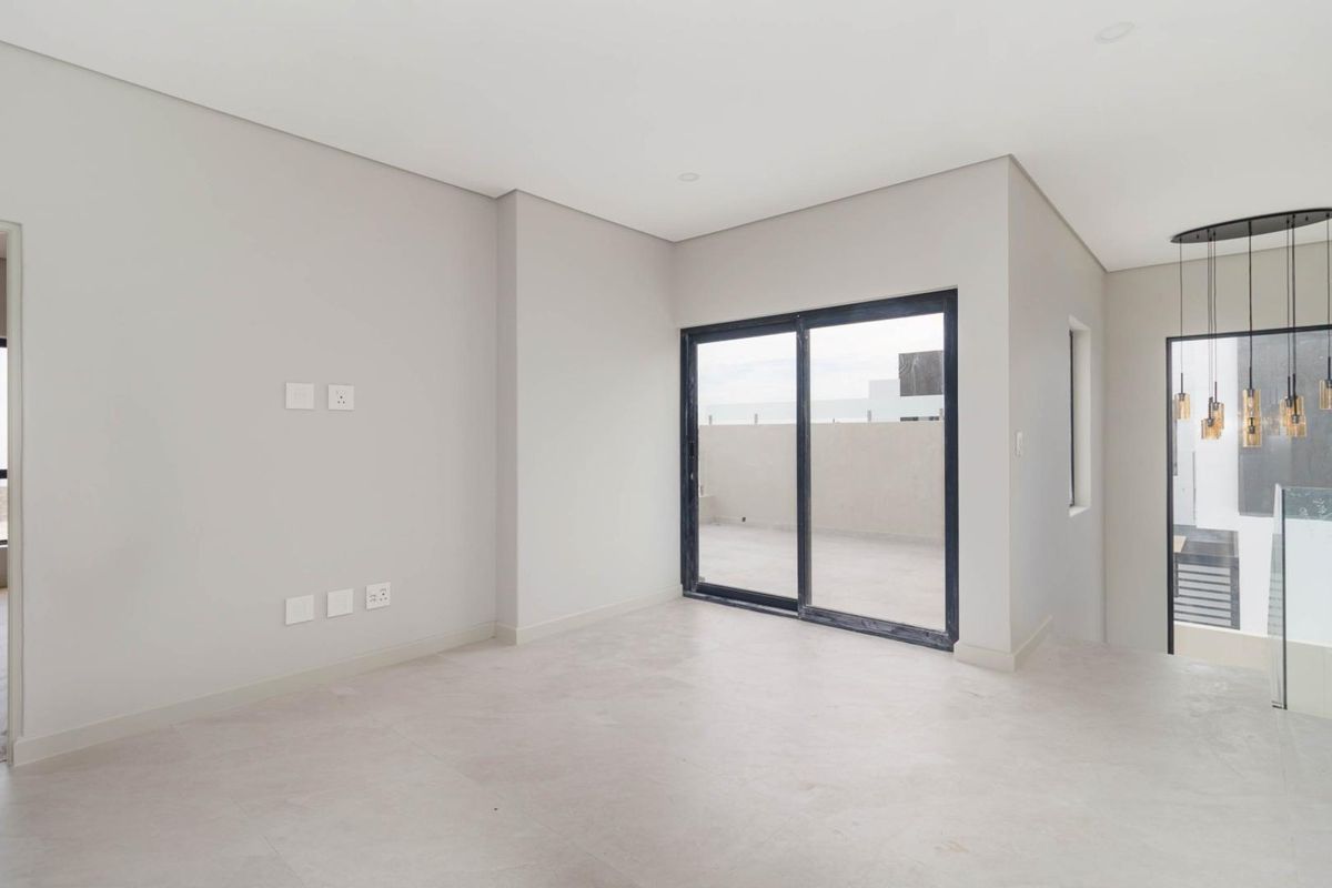 A bright, modern, and empty living area featuring neutral tiled flooring, recessed lighting, and sliding glass doors that open onto an outdoor balcony.