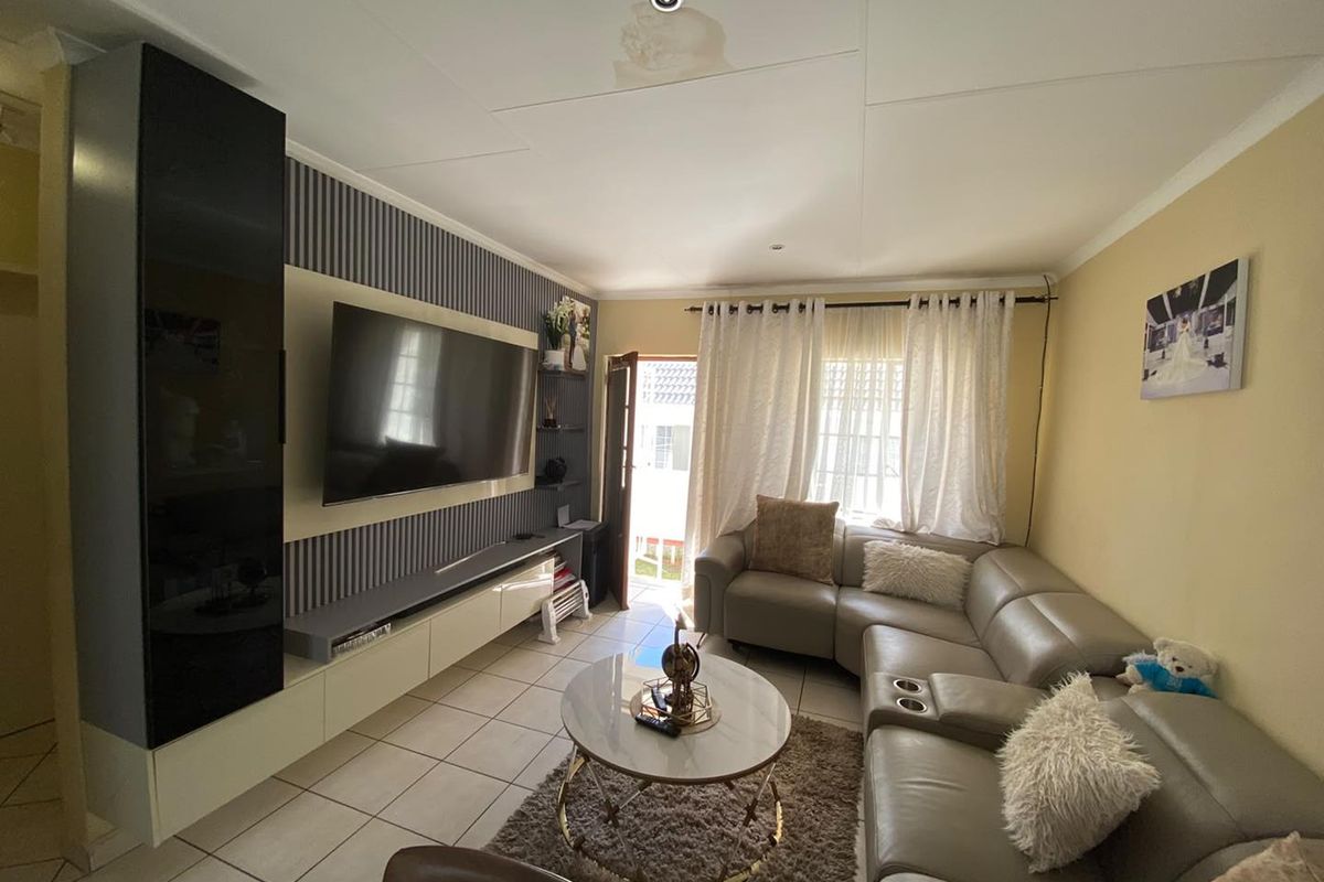 A living room featuring a built-in media unit, tiled flooring, and access to an outdoor area, showing a visible water stain on the ceiling.