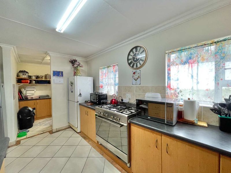 Functional kitchen featuring wooden cabinetry, gas stove, tiled backsplash, and an adjoining scullery area with additional storage space.