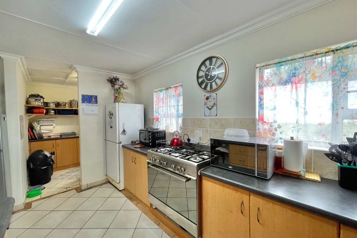 Functional kitchen featuring wooden cabinetry, gas stove, tiled backsplash, and an adjoining scullery area with additional storage space.