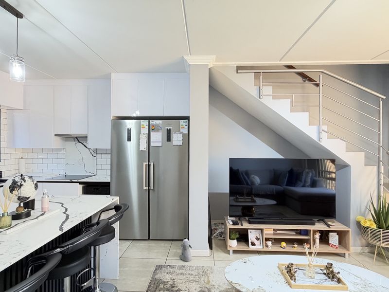 Modern open-plan living area featuring a sleek kitchen with marble-look island, subway tile backsplash, and a staircase with contemporary stainless steel railing.