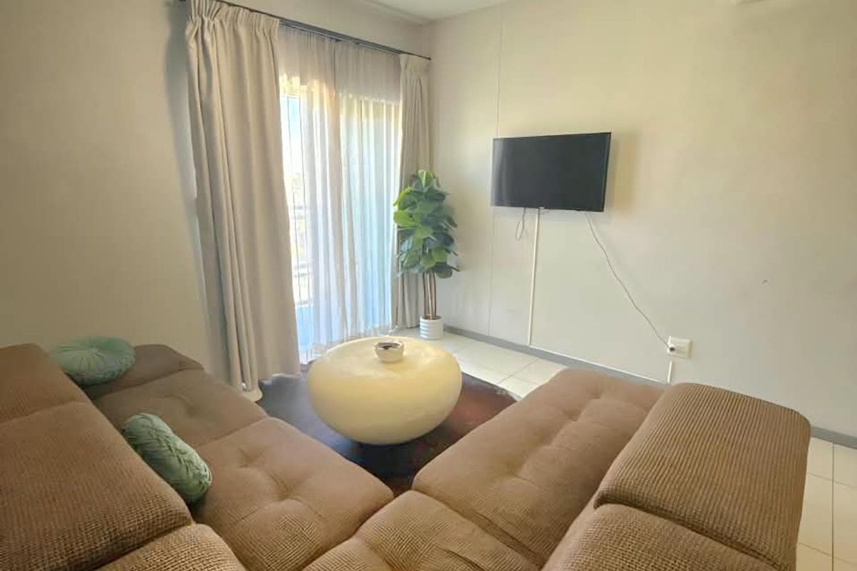 A comfortable living room featuring tiled flooring, a wall-mounted air conditioning unit, and a sliding glass door providing access to the exterior.