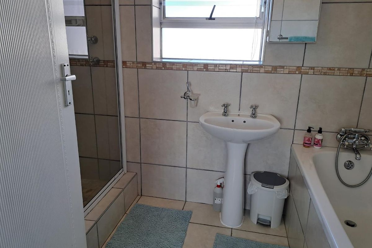 A functional bathroom featuring a pedestal basin, a bathtub with a handheld shower attachment, and a separate glass-enclosed shower stall with tiled walls.