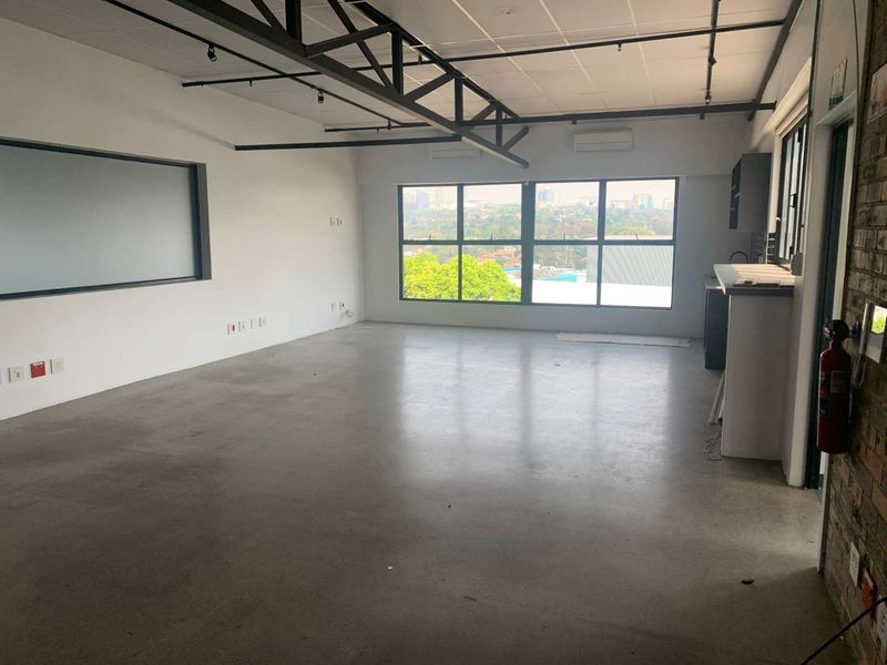 Spacious open-plan office featuring polished concrete floors, exposed steel roof trusses, split-system air conditioning, and a built-in kitchenette with expansive city views.