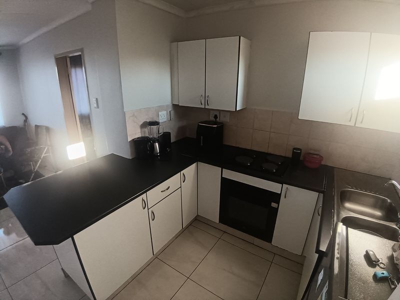 A functional kitchen featuring white cabinetry, black countertops, an integrated electric hob and oven, and a double stainless steel sink with tiled flooring.