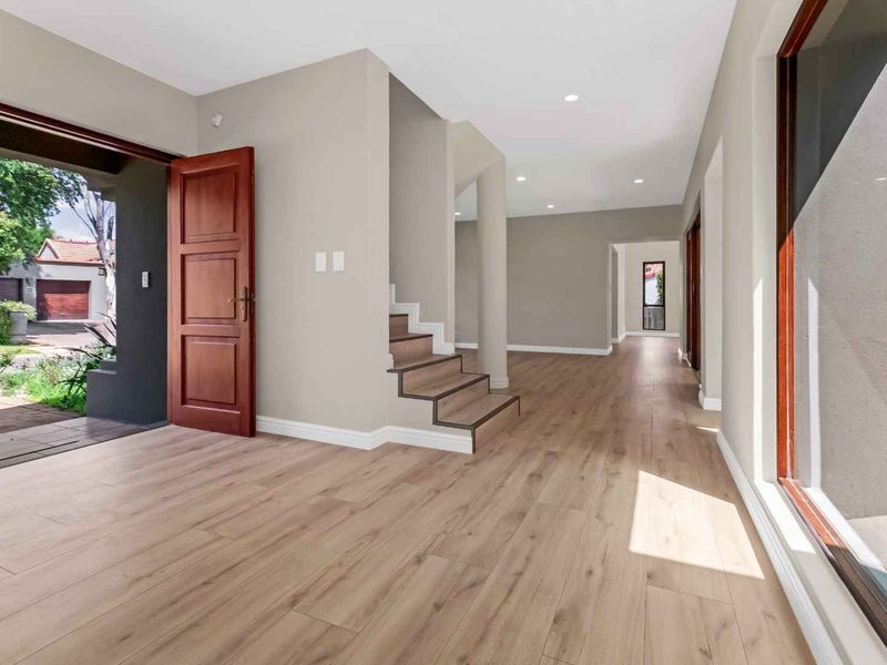 Bright and spacious entrance hall featuring modern laminate flooring, a timber staircase, and large windows providing natural light.