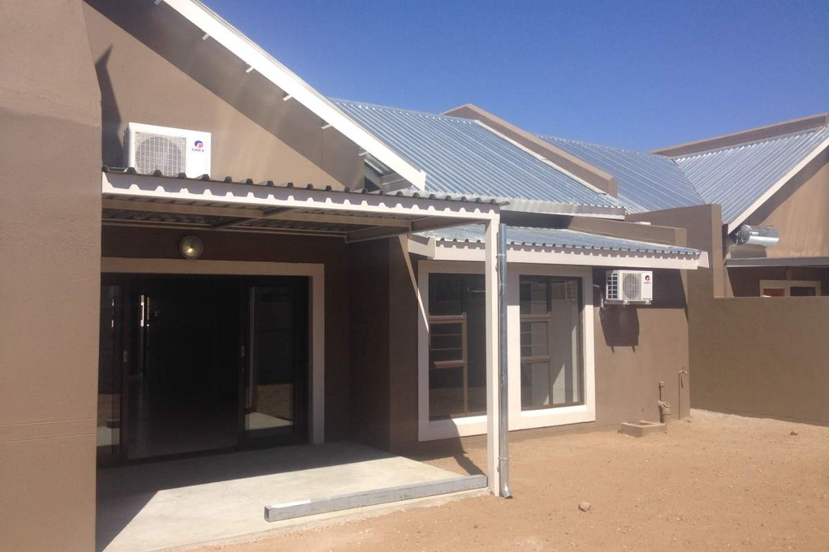 Rear view of a townhouse featuring a covered patio, sliding glass doors, corrugated metal roofing, and exterior air conditioning units.