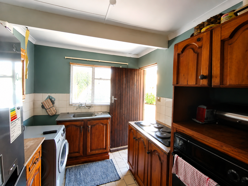 A functional kitchen featuring traditional wooden cabinetry, built-in oven and hob, tiled splashbacks, and direct access to the exterior.