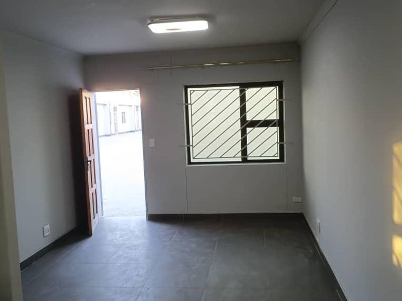 A clean, empty bedroom featuring tiled flooring, a window with security bars, and a simple ceiling light fixture.