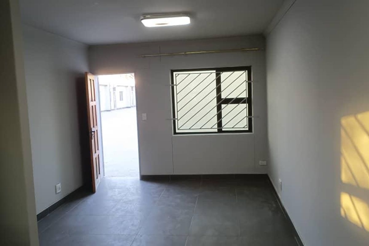 A clean, empty bedroom featuring tiled flooring, a window with security bars, and a simple ceiling light fixture.