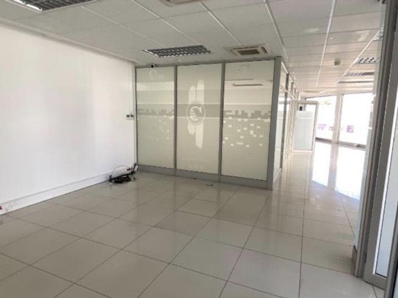 An empty, open-plan office space featuring tiled flooring, suspended ceilings with recessed lighting, and modern glass partition walls.
