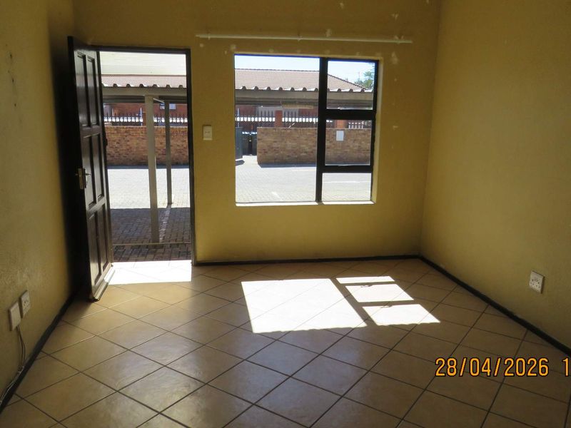 An empty living room featuring tiled flooring, natural light through an aluminium window, and direct access to the exterior parking area.