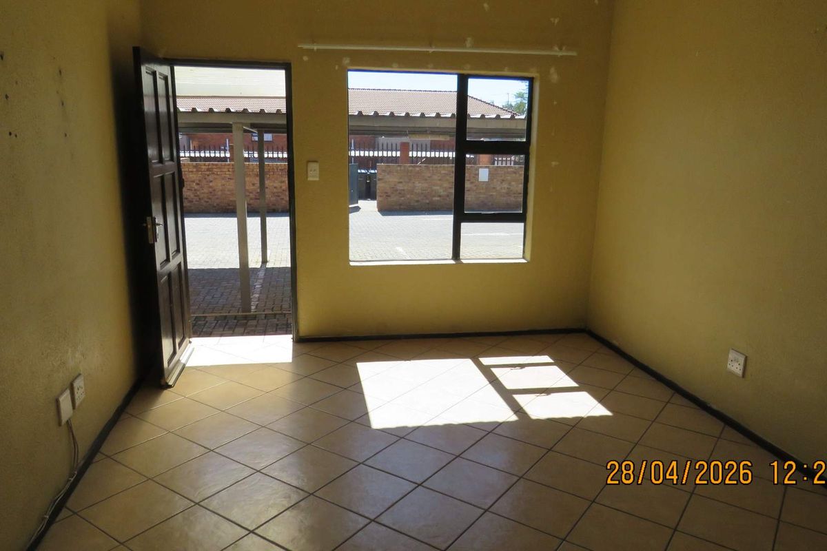 An empty living room featuring tiled flooring, natural light through an aluminium window, and direct access to the exterior parking area.