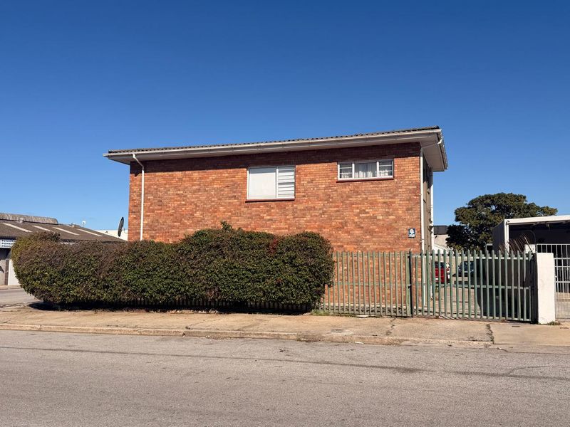 Side view of a brick apartment building featuring security fencing and established hedging along the perimeter.