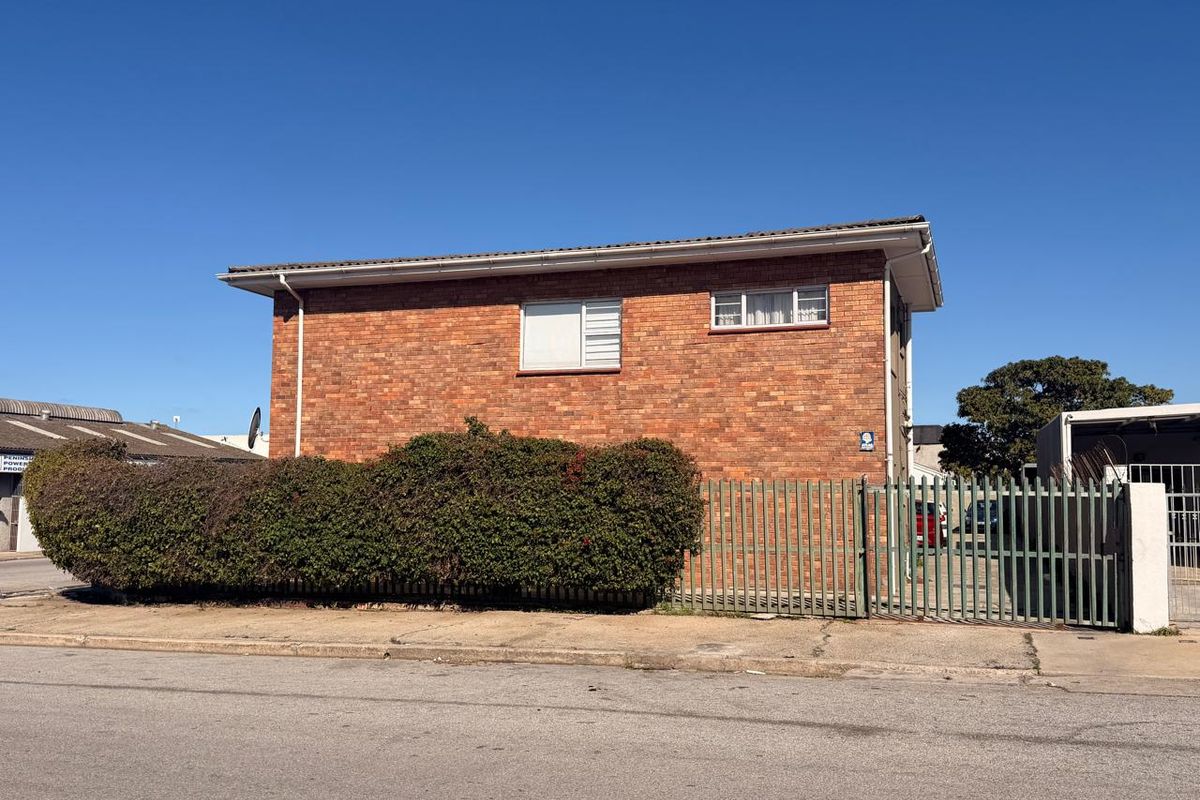 Side view of a brick apartment building featuring security fencing and established hedging along the perimeter.