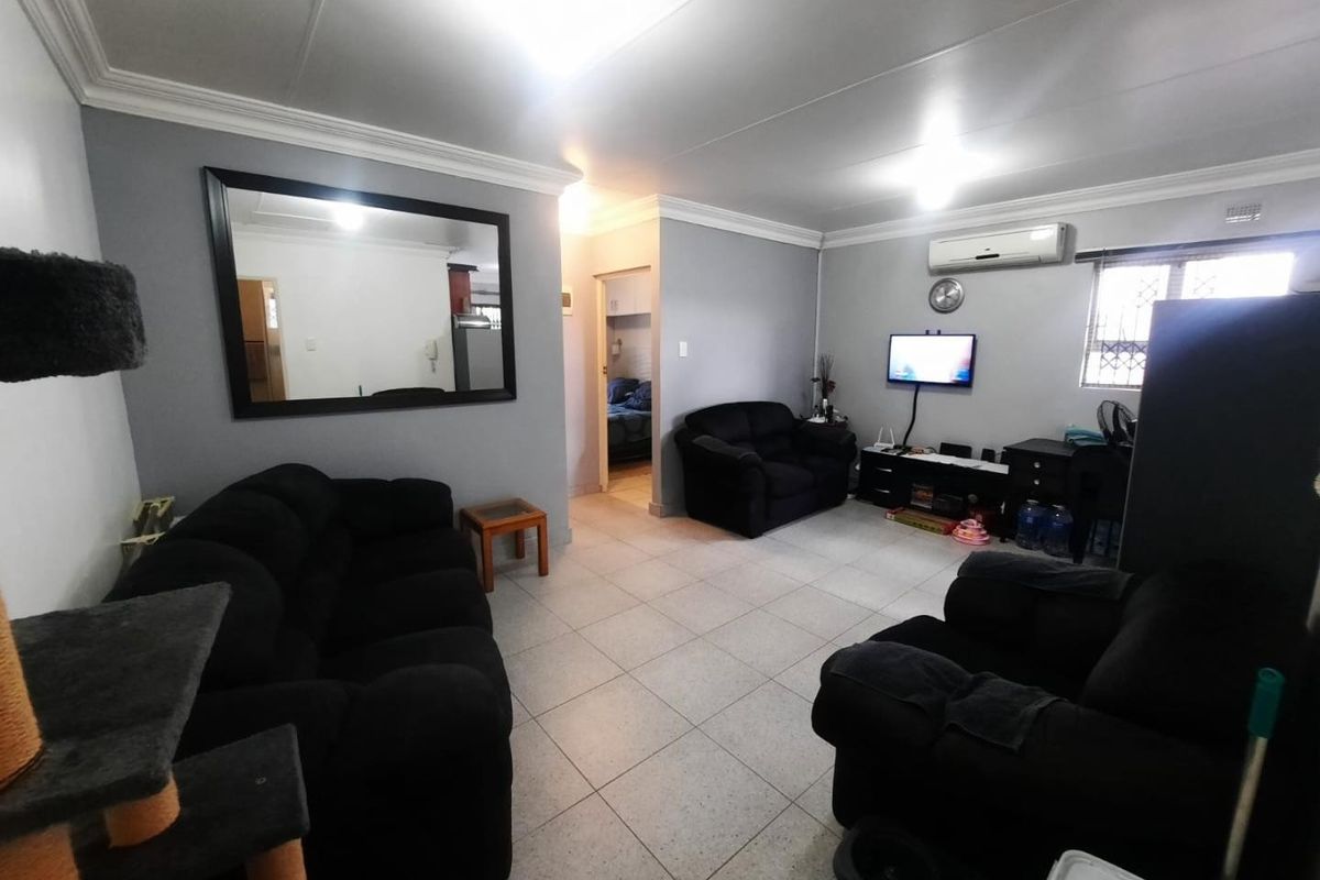 Spacious living room featuring tiled flooring, cornicing, and a wall-mounted air conditioning unit, providing a comfortable and functional living space.