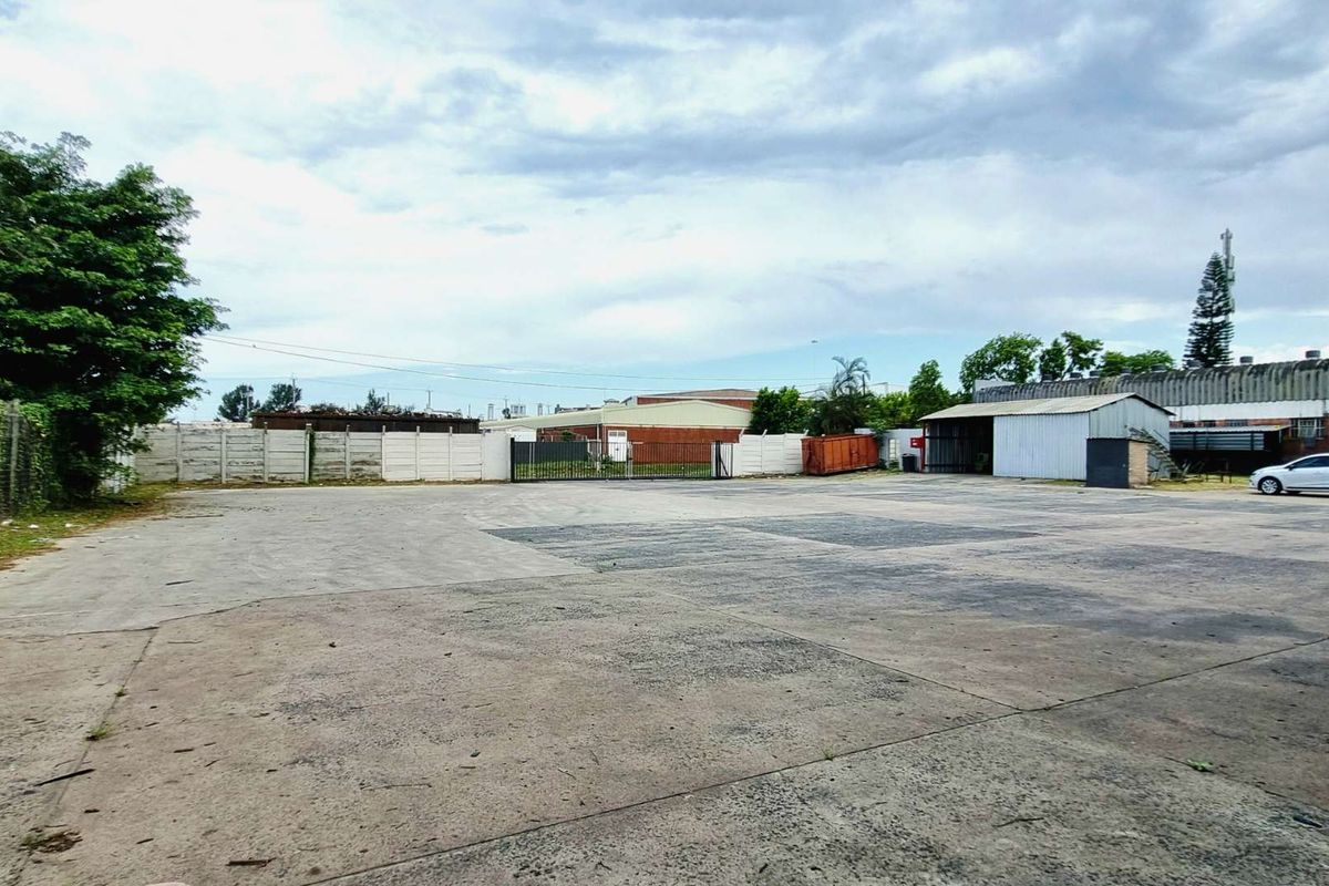 Expansive industrial yard featuring a large concrete paved area, perimeter fencing, and a metal-clad storage structure.